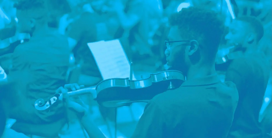 An image of a violinist on stage wearing a t-shirt and holding his violin to his shoulder. Image has a blue filter.