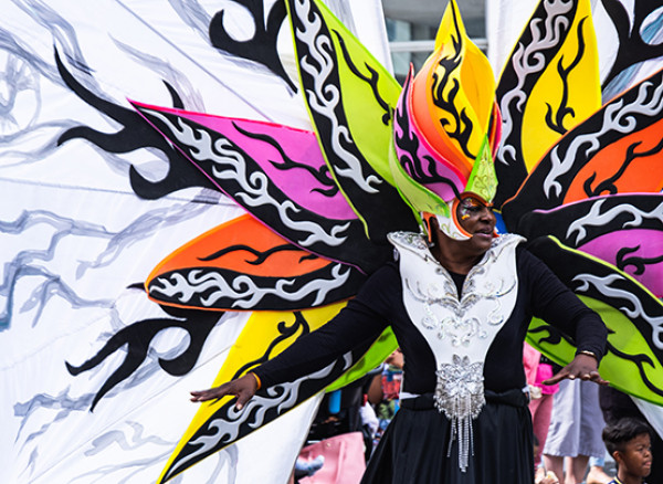 An image of a man wearing a black and silver body costume, with a mask which has long petal shapes in bright purple, ora