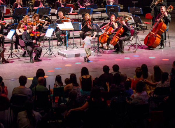 A young child runs in front of performing RPO musicians