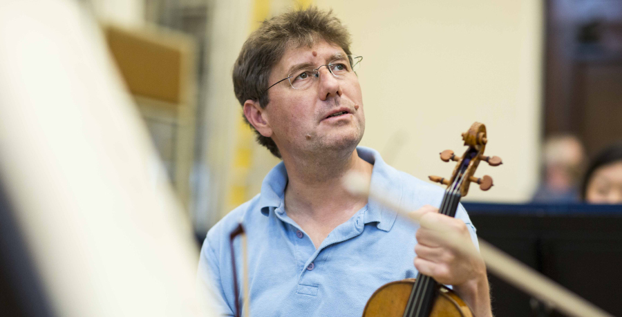 RPO Player Tamás András in rehearsal, holding his violin and looking up.